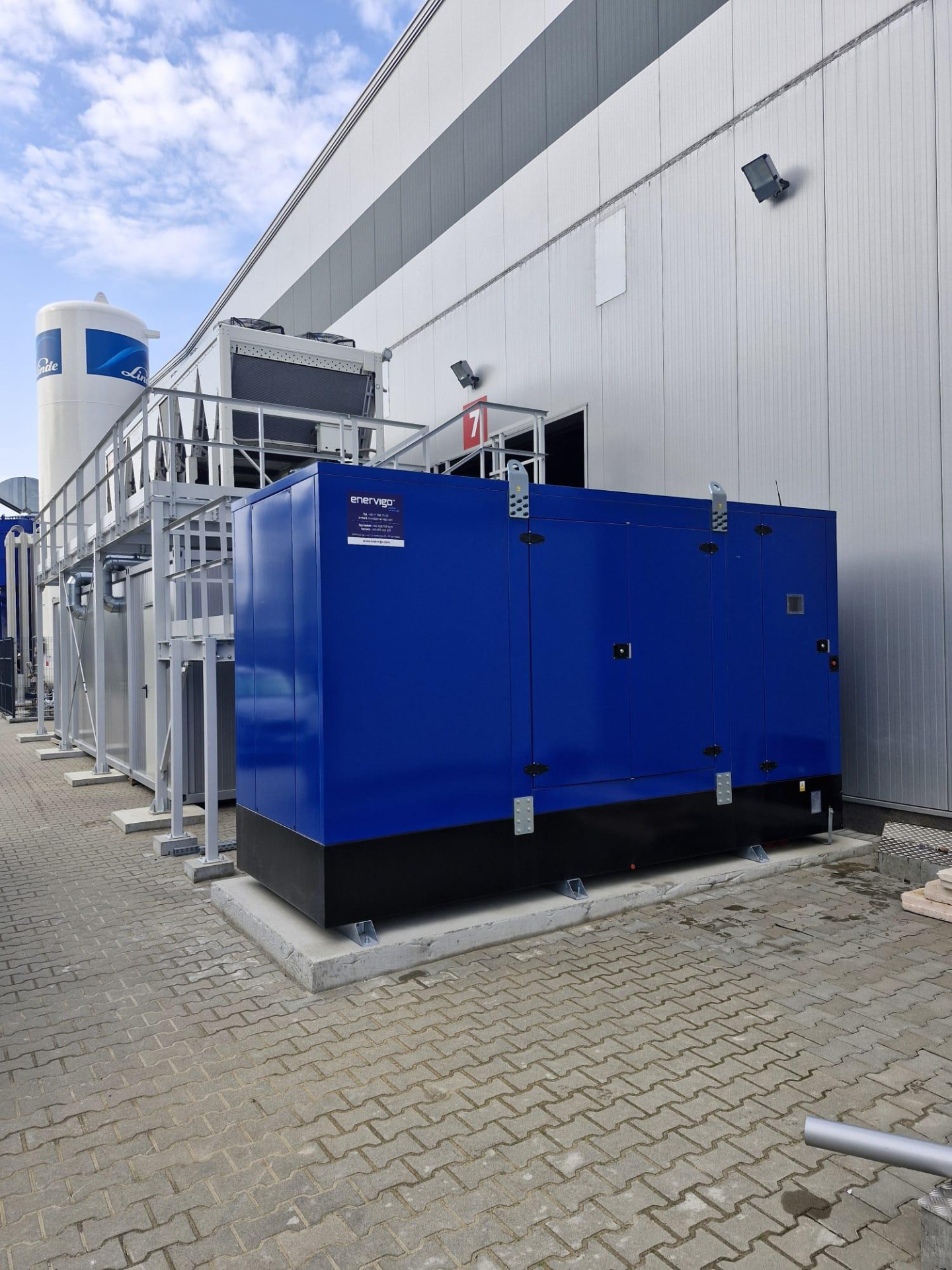 Agregat prądotwórczy diesel posadowiony na fundamencie, obok zakładu produkcyjnego.